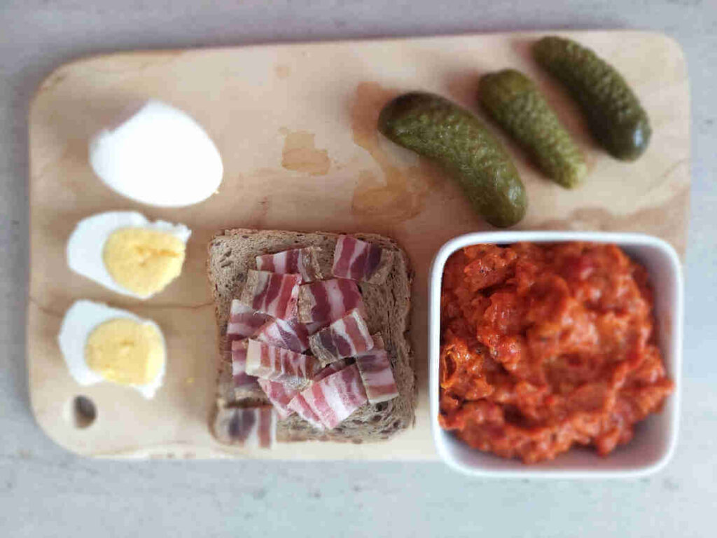 Ajvar served for breakfast with boiled eggs, bacon, and pickles