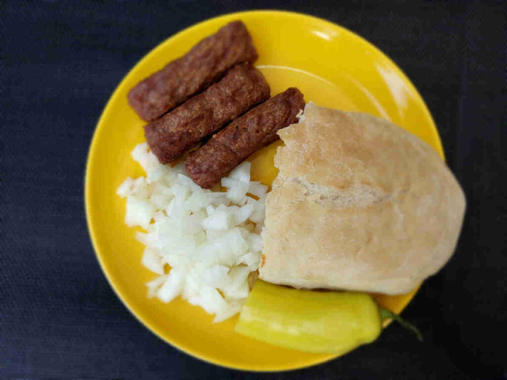 Ćevapi served with chopped onions, somun, and hot pepper