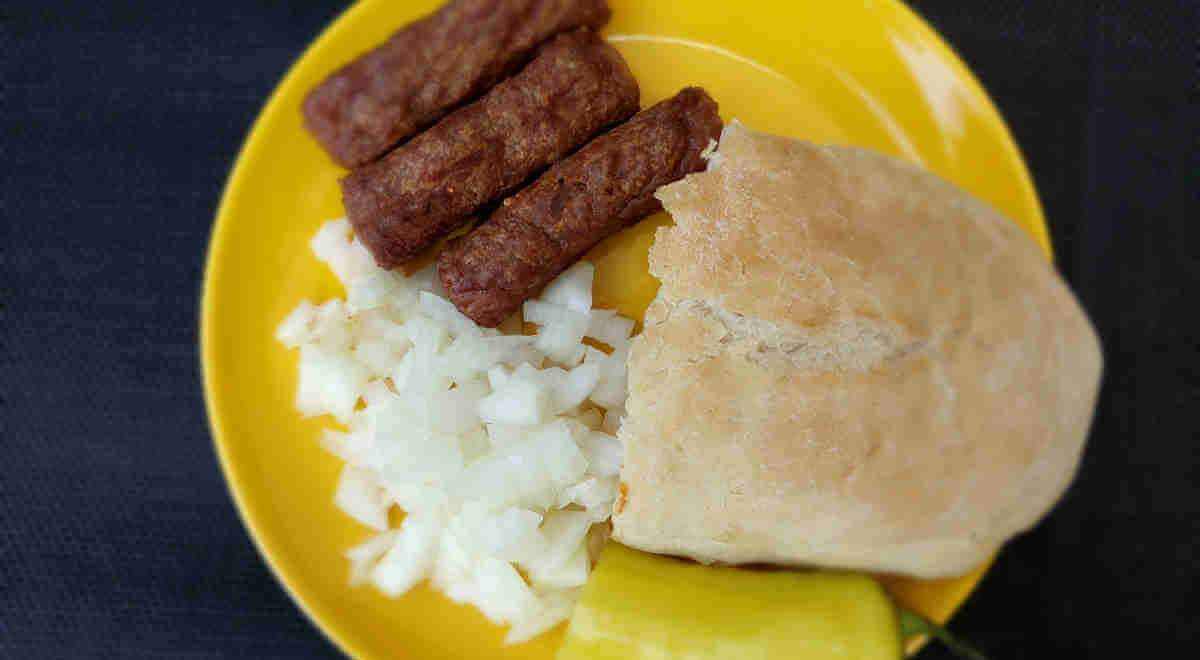 Ćevapi served with chopped onions, somun, and hot pepper