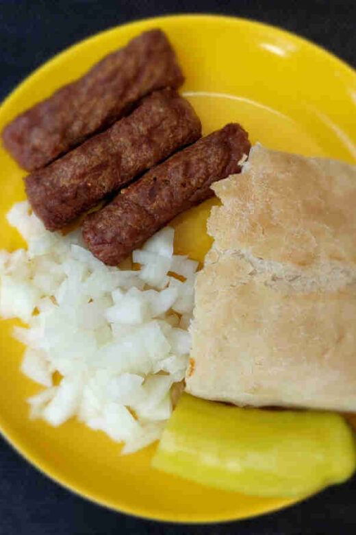 Ćevapi served with chopped onions, somun, and hot pepper